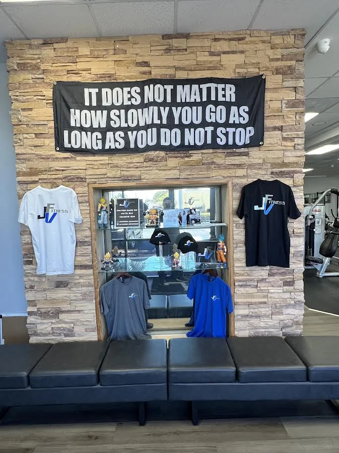 JV Fitness branded shirts and hoodies on a display wall with a motivational sign