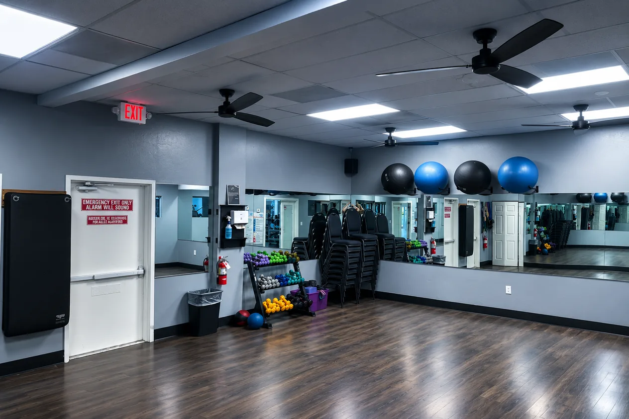 Mirrored studio room with wood floor, stability balls and a wall fan at JV Fitness